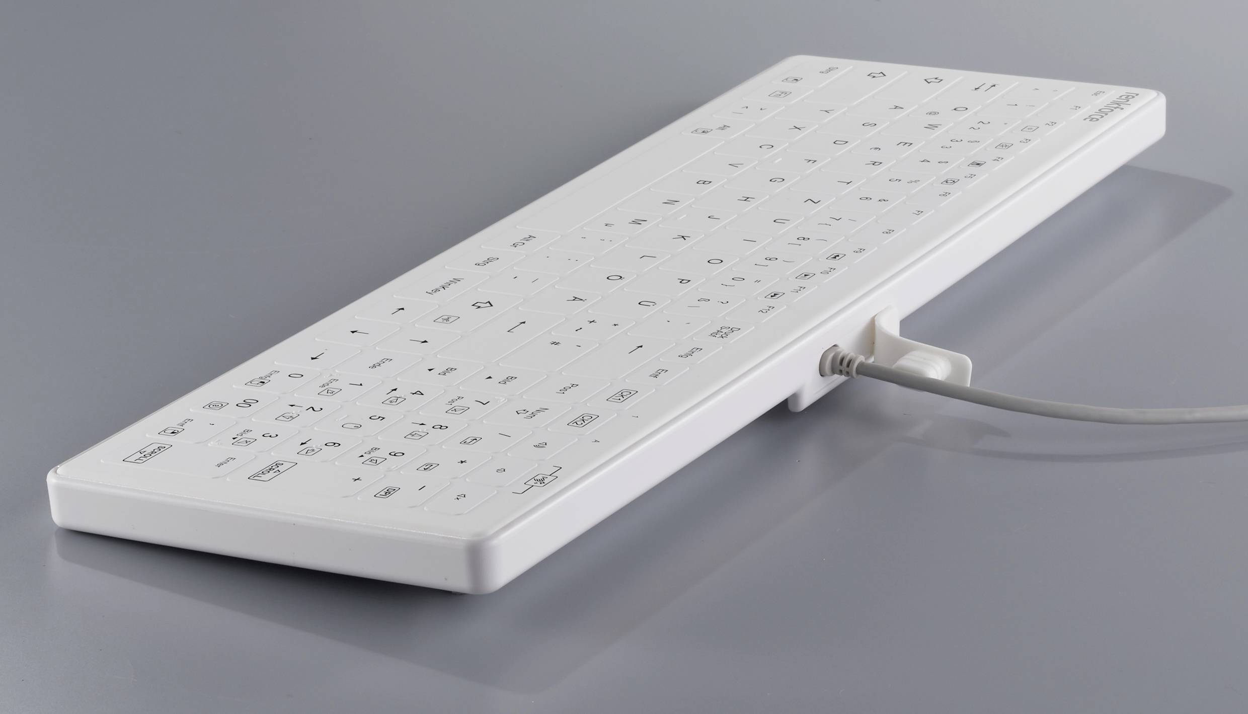 Weiße, flache Tastatur mit Kabel auf grauer Fläche. Die Tasten sind mit schwarzen Symbolen und Buchstaben bedruckt.
