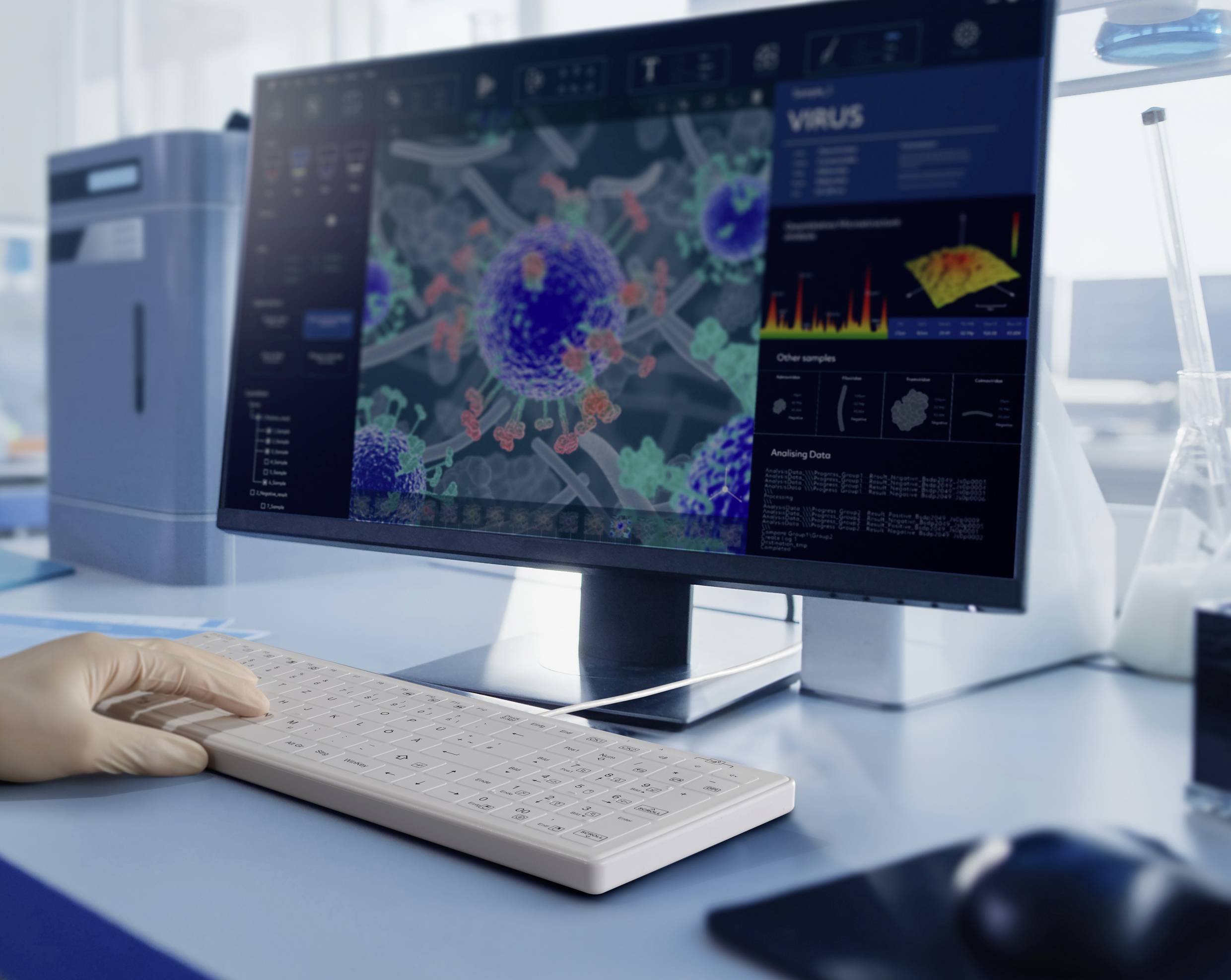 Eine Hand tippt auf eine Tastatur vor einem Monitor mit virologischen Daten und 3D-Darstellung eines Virus in einem Laborumfeld.