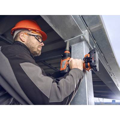 Ein Arbeiter mit Schutzbrille und Helm befestigt Metallbalken mit einer Bohrmaschine an einer Stahlkonstruktion.