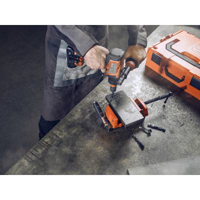 Eine Person bohrt mit einer elektrischen Bohrmaschine in eine Metallplatte, die auf einem Schraubstock befestigt ist. Nebenbei liegt ein orangefarbener Werkzeugkoffer.