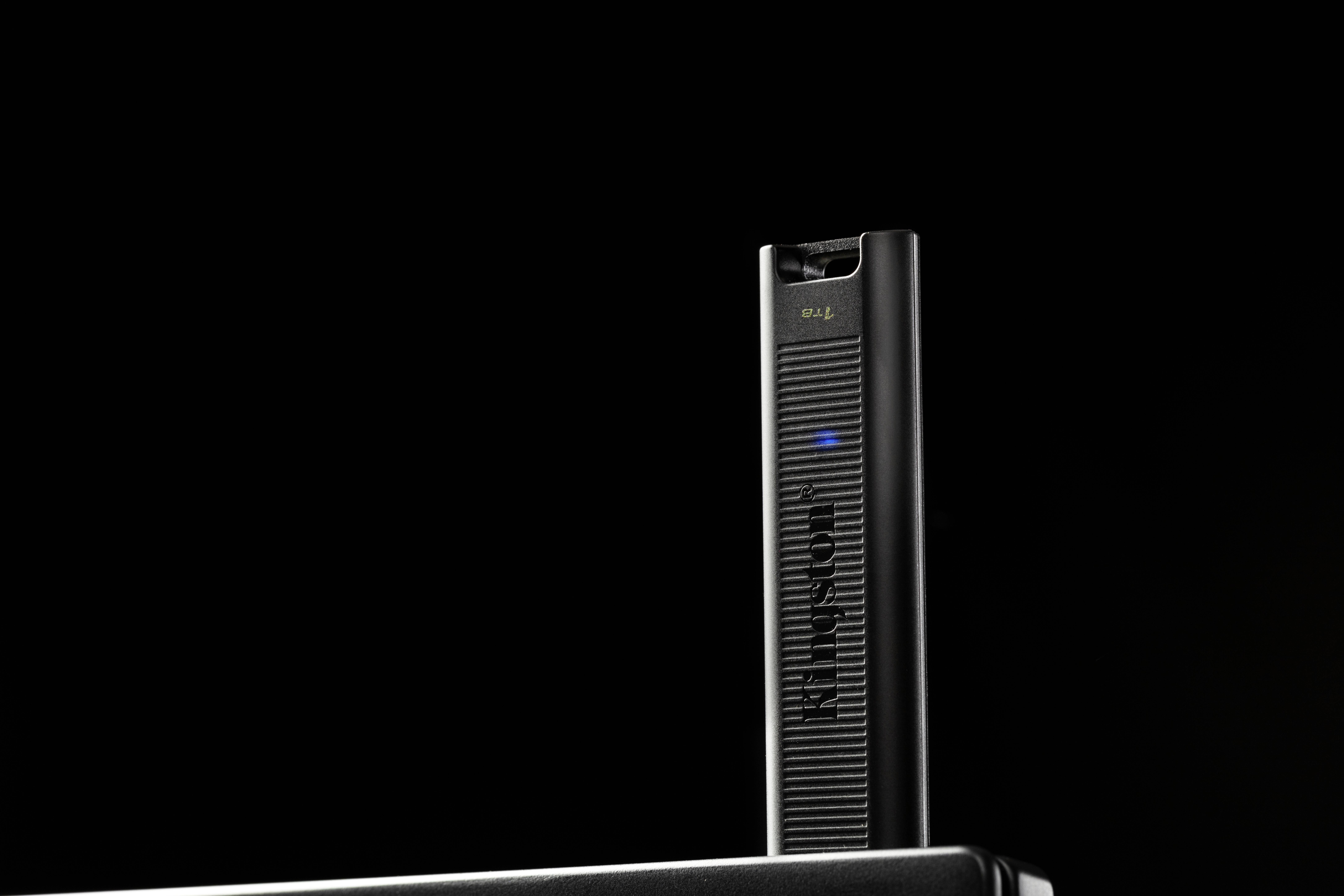 Eine schwarze E-Zigarette mit blau leuchtender Anzeige steht aufrecht auf dunklem Hintergrund.