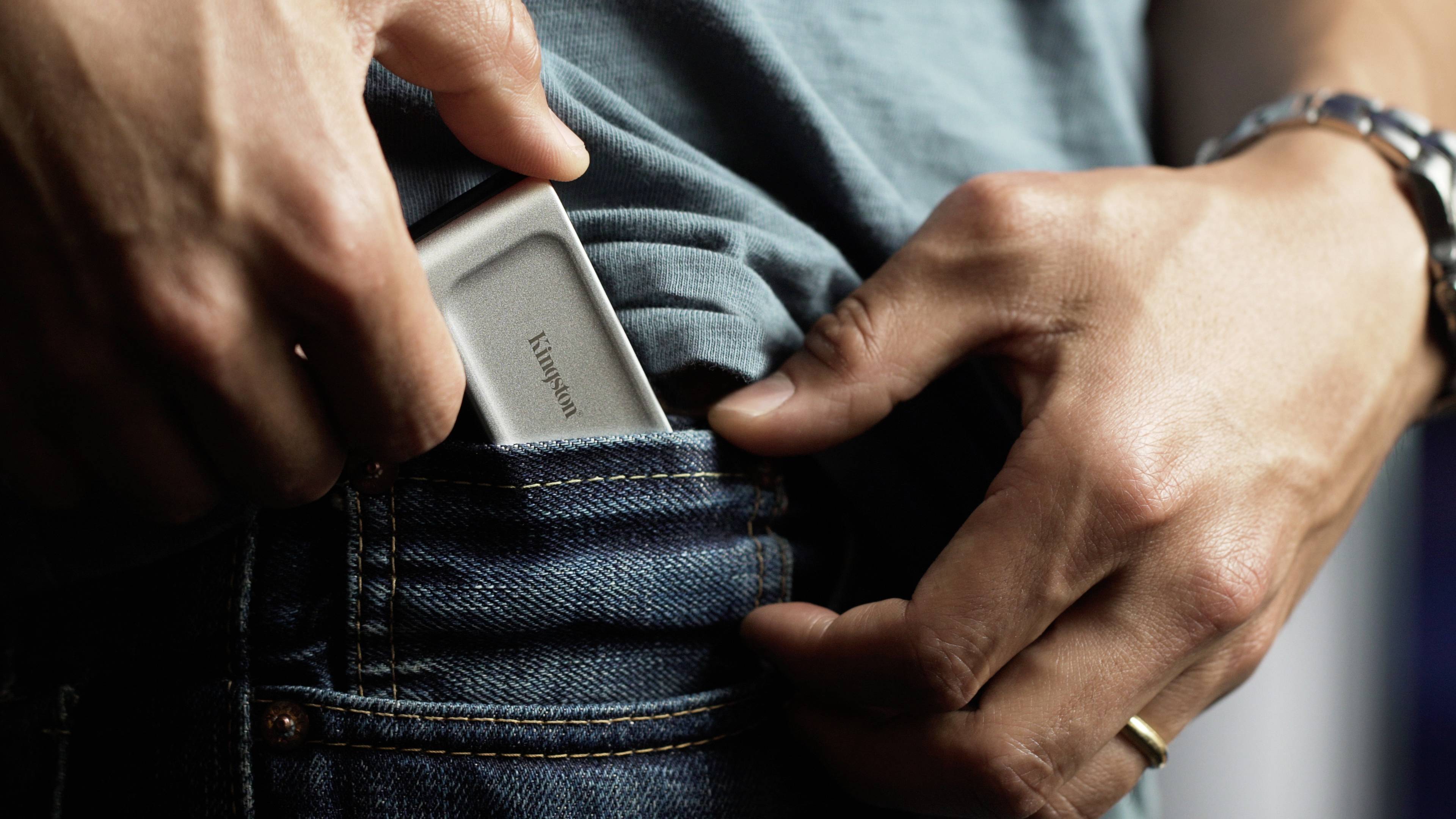 Eine Person steckt ein kleines, rechteckiges Gerät in die Gesäßtasche einer Jeans.