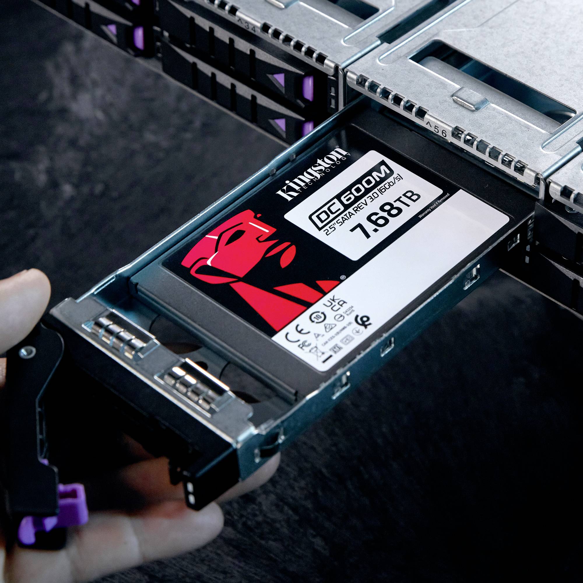 Eine Hand hält eine herausgezogene SSD mit der Aufschrift 'Kingston DC600M 7.68TB', eingebaut in einen Server-Rack-Schacht.