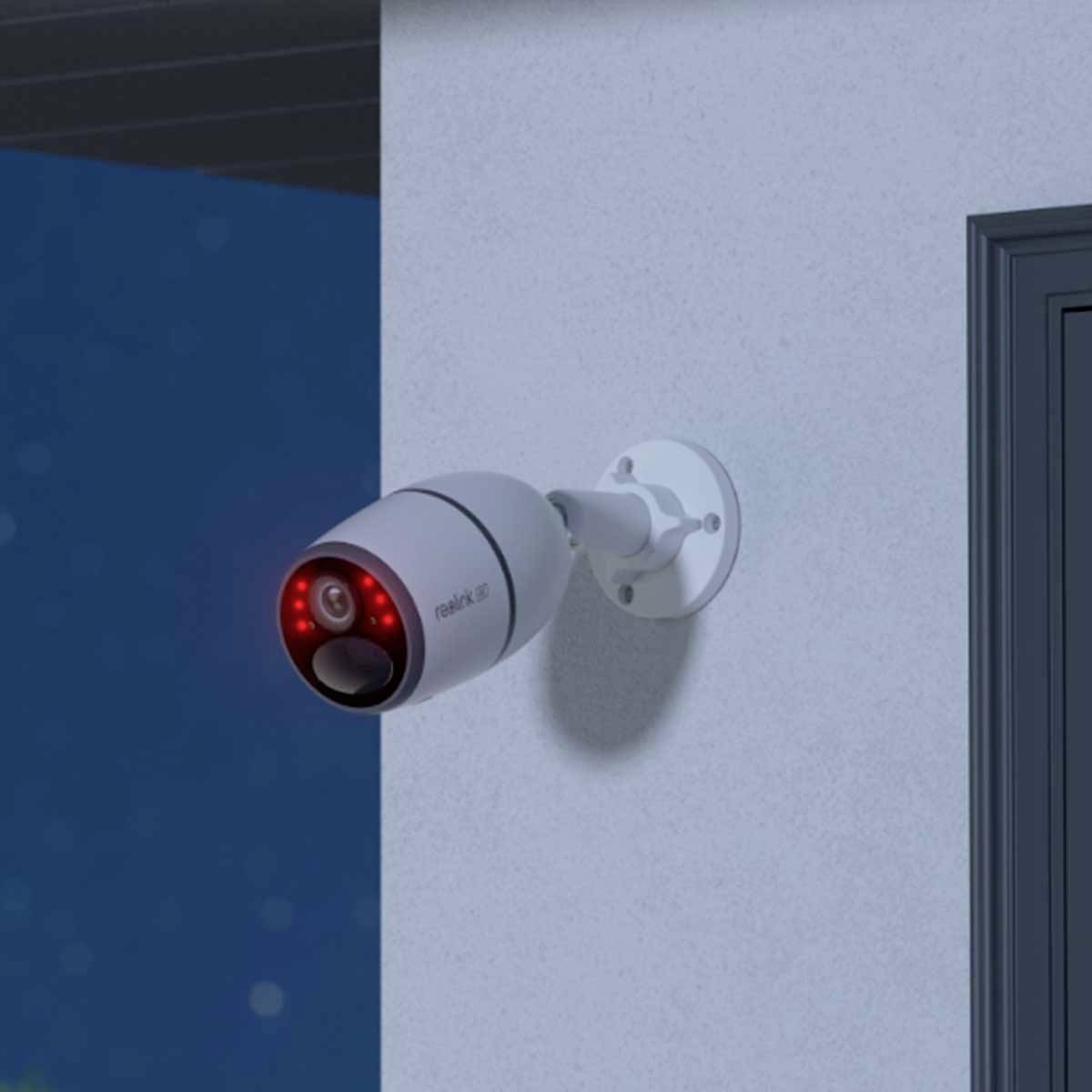 Eine Überwachungskamera ist an einer Hauswand montiert. Die Kamera leuchtet rot und ist auf einen Außenbereich gerichtet.