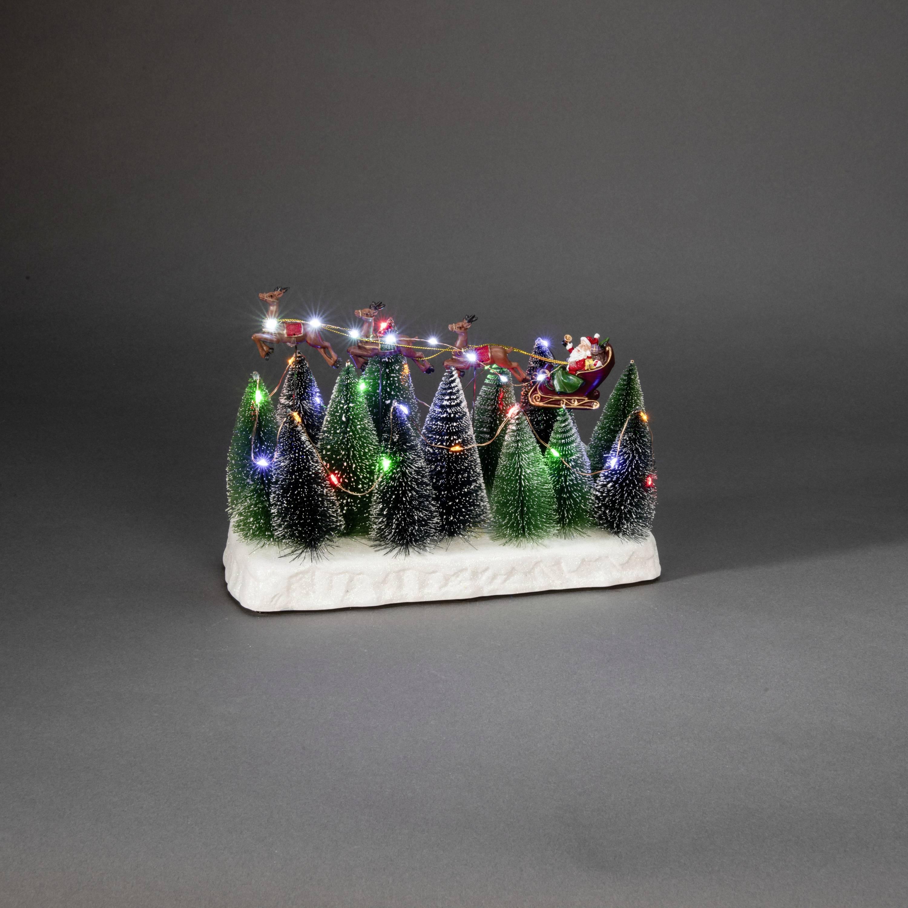 Weihnachtsszene: Miniatur-Bäume mit bunten Lichtern, leuchtender Schlittenzugszene oben mit Rentieren und Weihnachtsmann auf Schneeunterlage.
