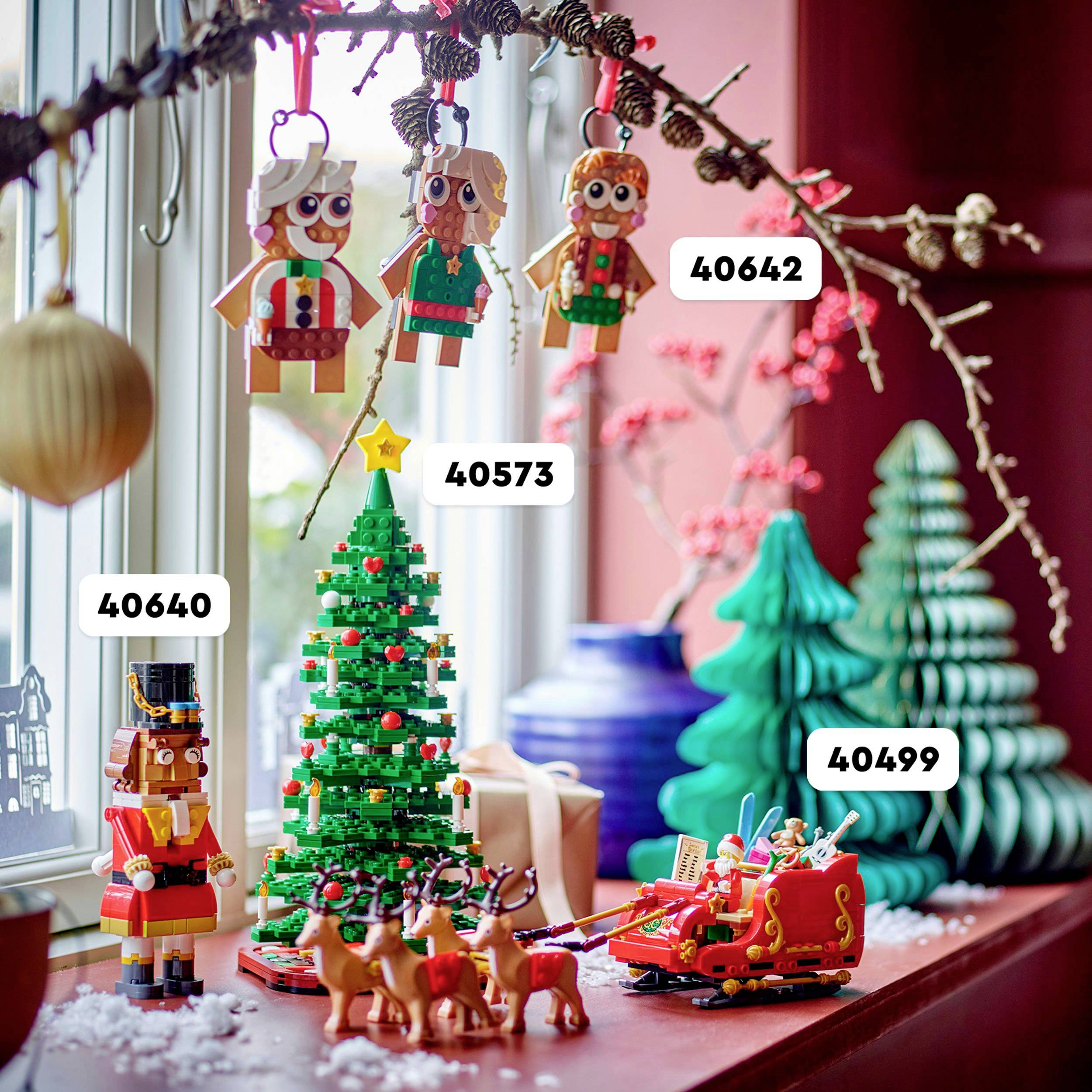Ein Fensterbrett mit einem Weihnachtsbaum, drei hängenden Figuren und weiteren LEGO-Weihnachtsszenen. Set-Nummern sind sichtbar.