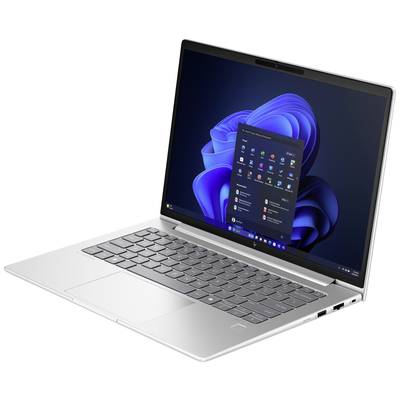 Silberner Laptop mit geöffneter Windows 11 Startmenü-Bildschirmansicht auf blauem Hintergrund, auf einem weißen Tisch stehend.