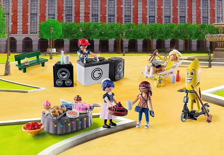 Spielzeugfiguren in einem Park. Eine DJ-Figur spielt Musik, andere Figuren verkleidet als Banane und Kuchen; Picknick-Szene.