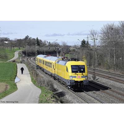 Ein gelber Zug der Deutschen Bahn fährt auf einer zweigleisigen Strecke durch eine ländliche Umgebung, Bäume rechts, ein Mann links.
