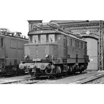 Eine alte elektrische Lokomotive steht vor einem Backsteingebäude in einem Bahndepot, schwarz-weiß-Foto.