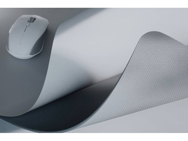 Eine weiße Computermaus auf einer grauen Schreibtischunterlage mit einem leicht aufgerollten Rand.