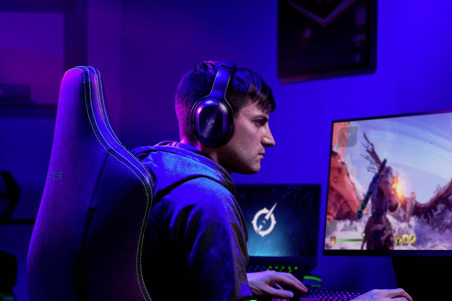 Ein Gamer mit Kopfhörern sitzt konzentriert vor einem Computerbildschirm, auf dem ein actionreiches Videospiel zu sehen ist.