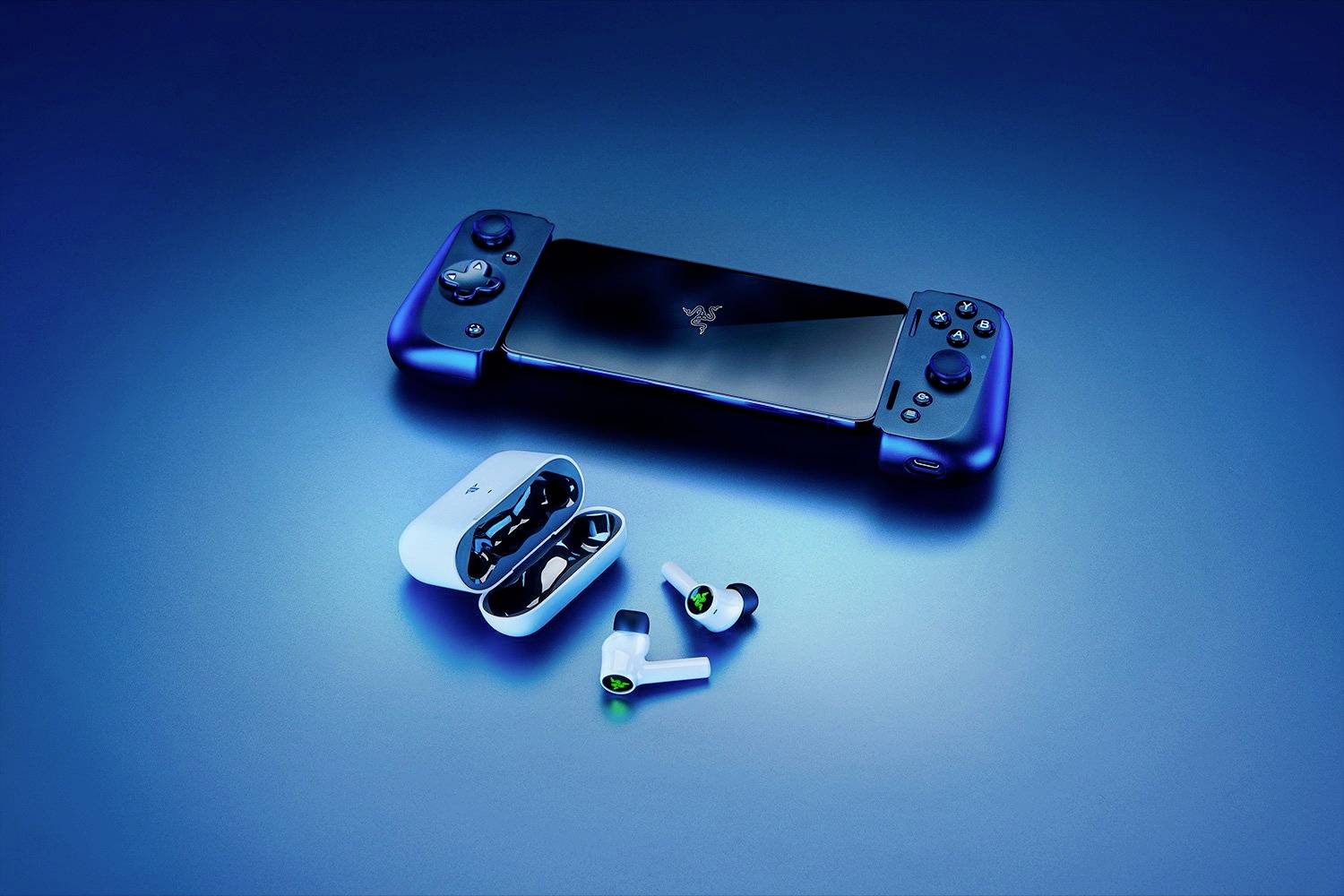 Ein schwarzer tragbarer Gaming-Controller mit blauen Griffen liegt neben einer offenen Hülle mit kabellosen Ohrhörern auf blauem Hintergrund.