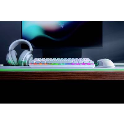 Eine beleuchtete Gaming-Tastatur, Maus und Kopfhörer auf einem Holzschreibtisch vor einem unscharfen Bildschirm.