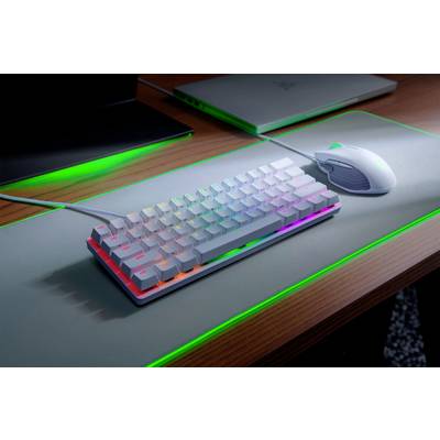 Tastatur mit Regenbogen-Beleuchtung und kabelgebundene Maus auf Schreibtischunterlage, neben aufgeklapptem Laptop.