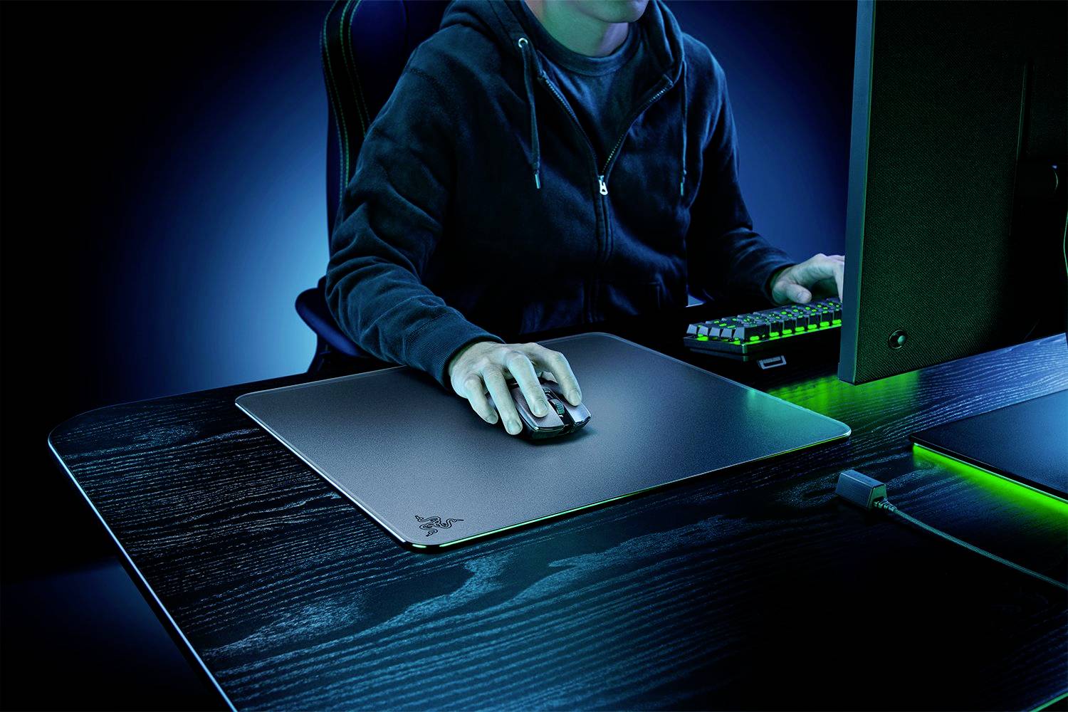 Eine Person in einem dunklen Raum benutzt einen Computer. Die Tastatur und das Mauspad leuchten in grünem Licht.