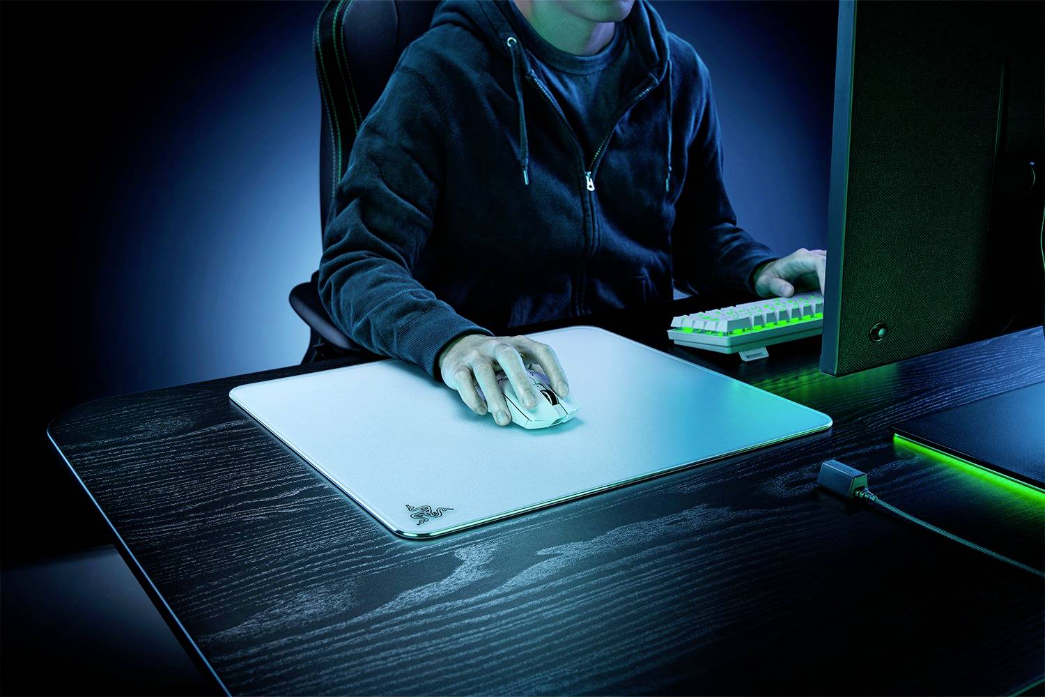 Eine Person in einem dunklen Hoodie benutzt einen Computer. Die Szene ist blau beleuchtet, betont Techniknutzung in einer modernen Umgebung.