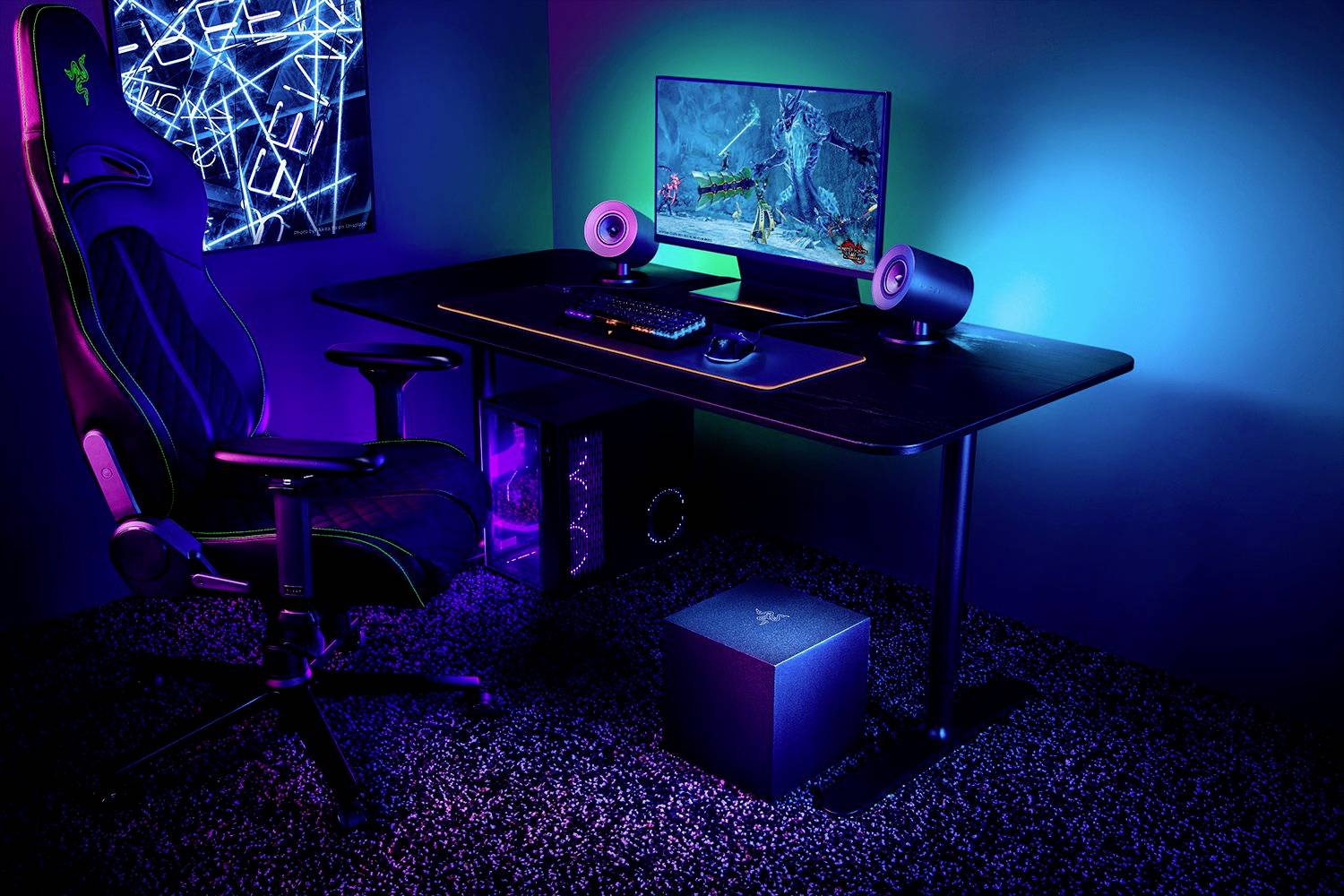 Ein moderner Gaming-Schreibtisch mit Computer, Monitor, Lautsprechern und beleuchtetem Gaming-Stuhl in einem blau beleuchteten Raum.
