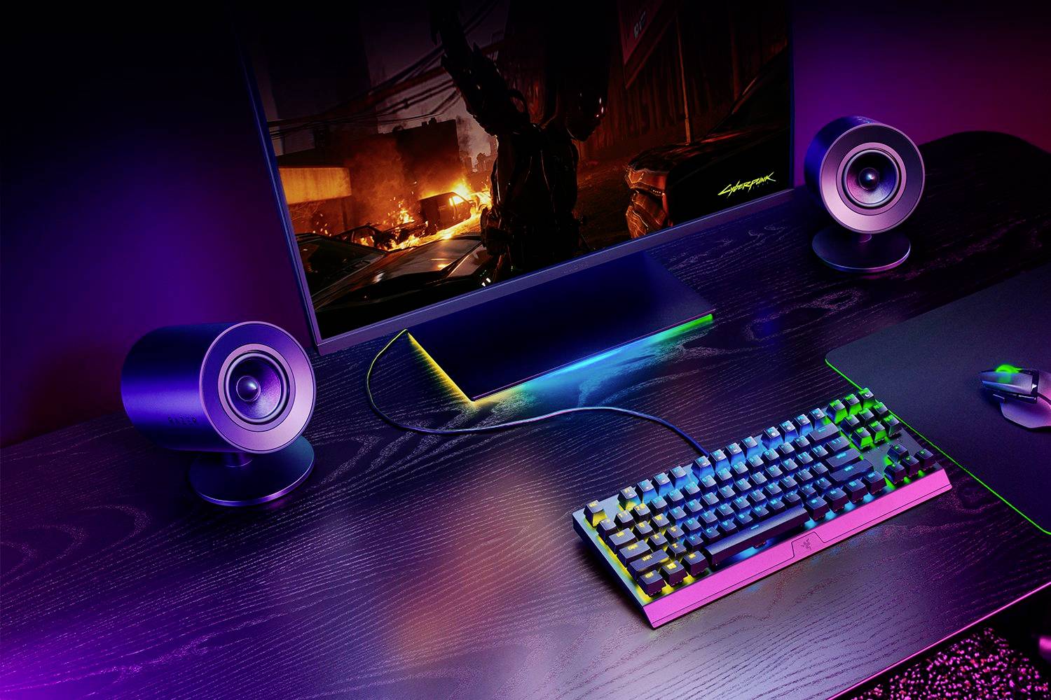 Ein beleuchteter Gaming-Schreibtisch mit Monitor, zwei Lautsprechern, einer Tastatur und einer Maus. Auf dem Monitor läuft ein Videospiel.