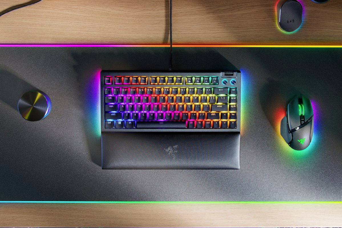 Eine beleuchtete Gaming-Tastatur mit RGB-Farben auf einem Schreibtisch. Daneben befinden sich eine Maus und ein Lautstärkeregler.