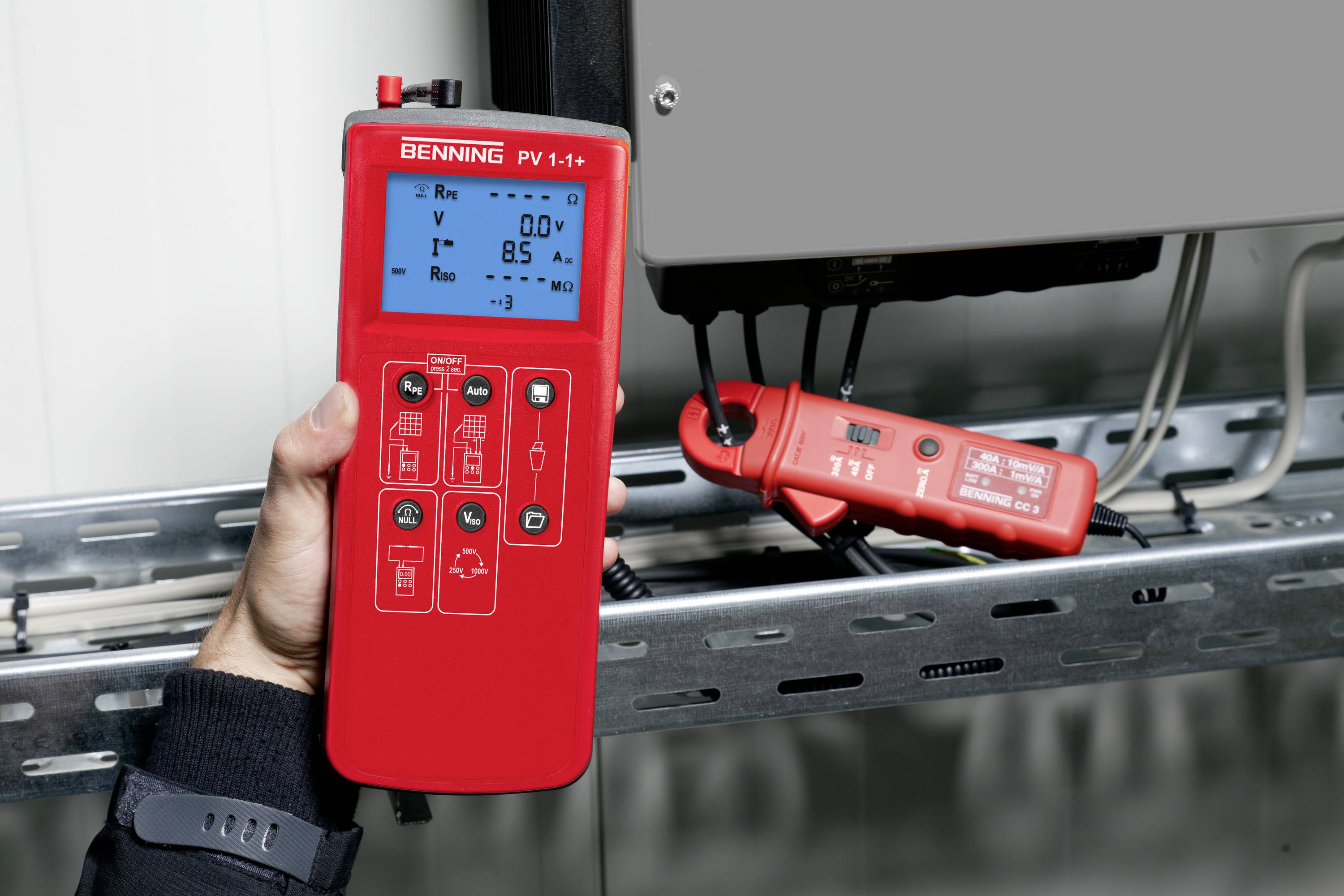 Eine Hand hält ein rotes Photovoltaik-Testgerät, das mit einem Solarpanel verbunden ist. Das Display zeigt Spannungs- und Strommessungen an.