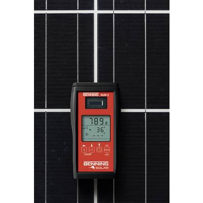Ein rotes Gerät mit Display zeigt '789' und '36°' an, angelehnt an eine Solarmoduloberfläche, vermutlich zur Leistungsmessung.