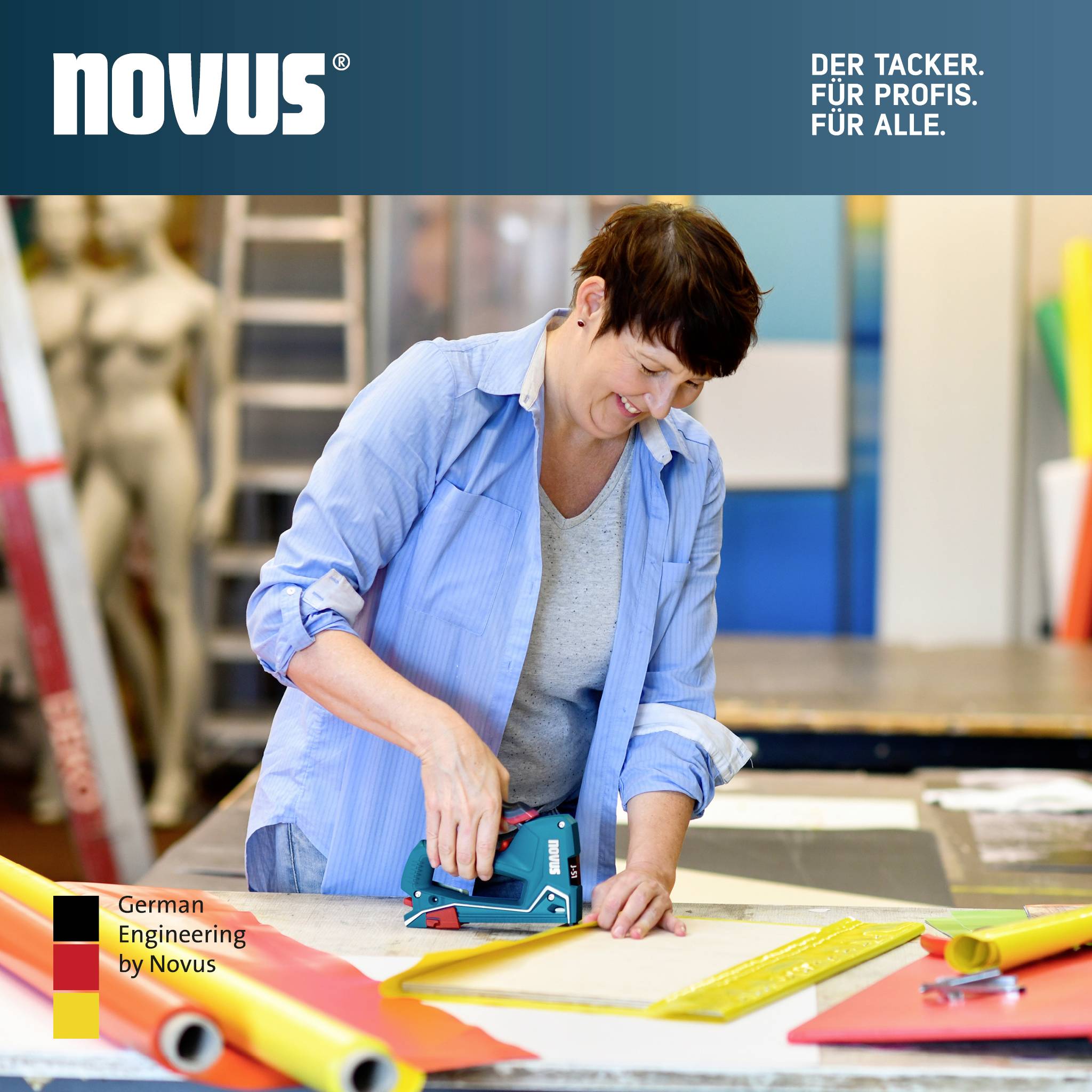 Frau tackert buntes Papier in einer Werkstatt. Oben steht: 'Der Tacker. Für Profis. Für alle.' Links unten: 'German Engineering by Novus'.