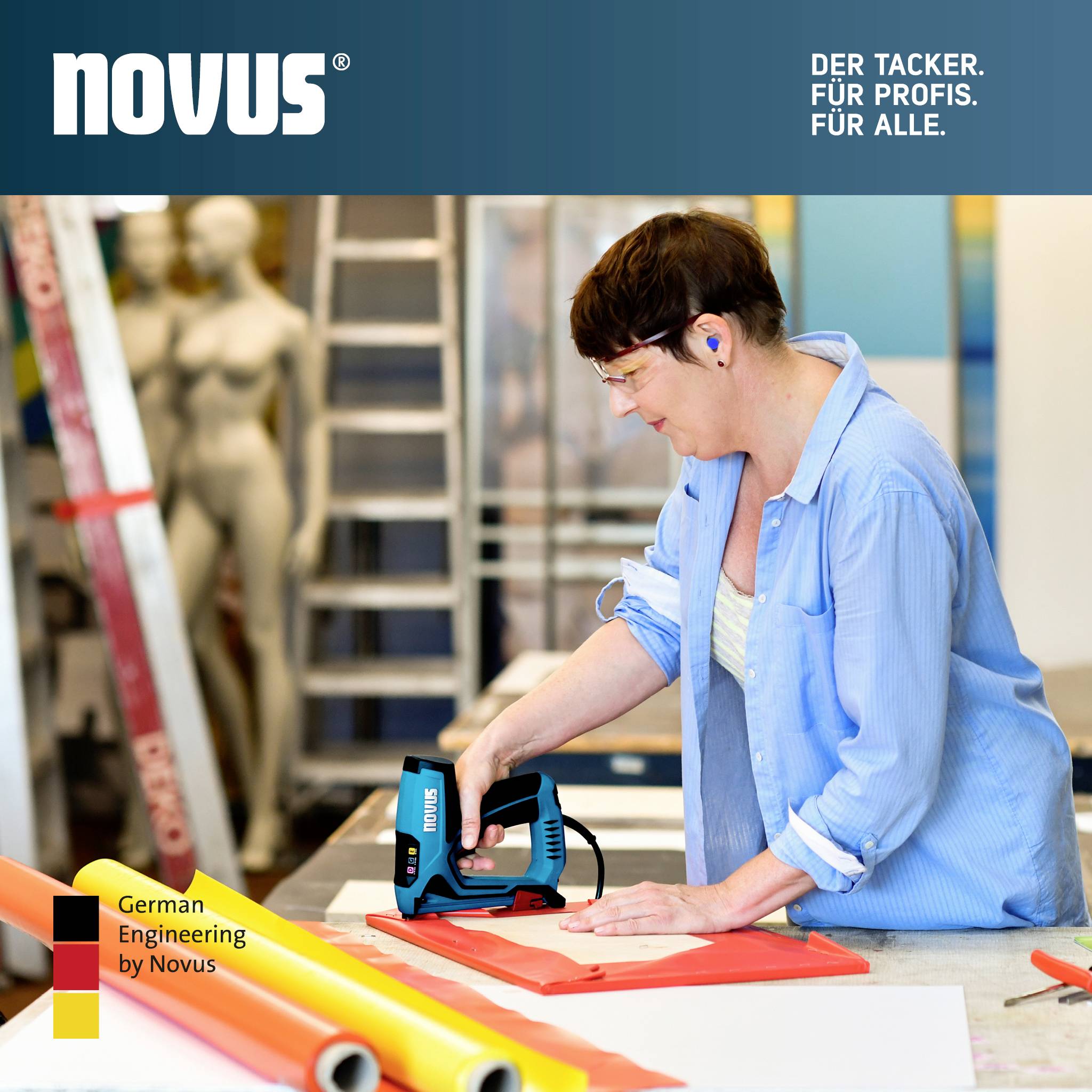 Eine Person betrachtet einen Novus-Tacker. Im Hintergrund sind Leitern sowie farbige Plakate zu sehen. Entworfen von Novus mit 'German Engineering'.