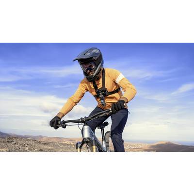 Ein Mann in Schutzkleidung fährt ein Mountainbike auf einem Hügel bei klarem Himmel. Der Hintergrund zeigt eine weite, offene Landschaft.