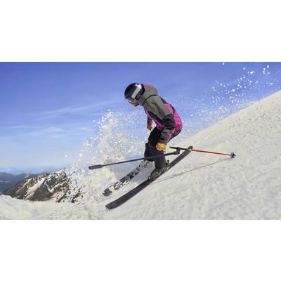 Skifahrer in rot-schwarzer Kleidung fährt dynamisch einen verschneiten Berghang hinunter, wirbelt Schnee auf, blauer Himmel im Hintergrund.