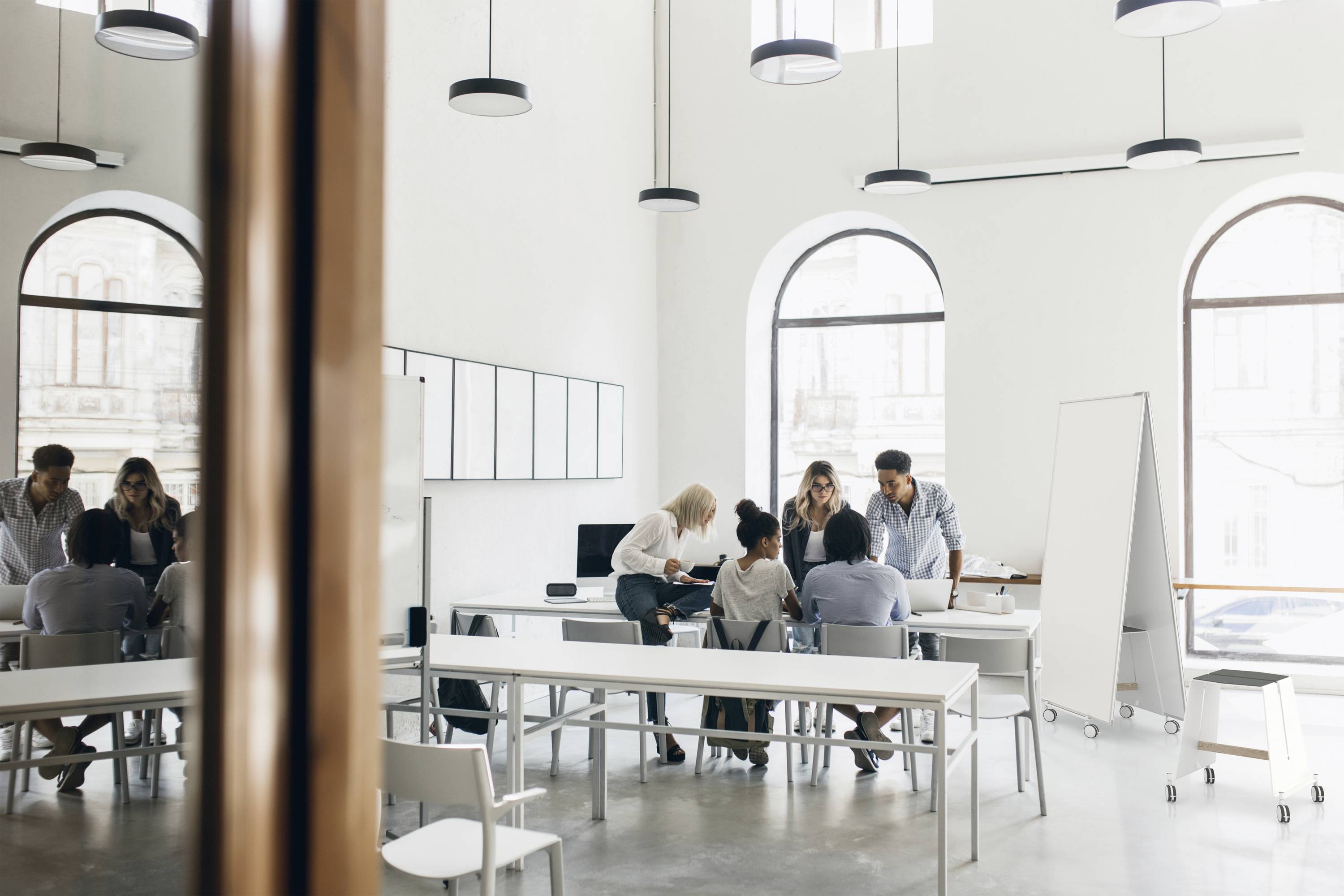 Eine Gruppe von Menschen arbeitet in einem modernen Büro mit großen Fenstern zusammen. Ein großes Whiteboard steht bereit.