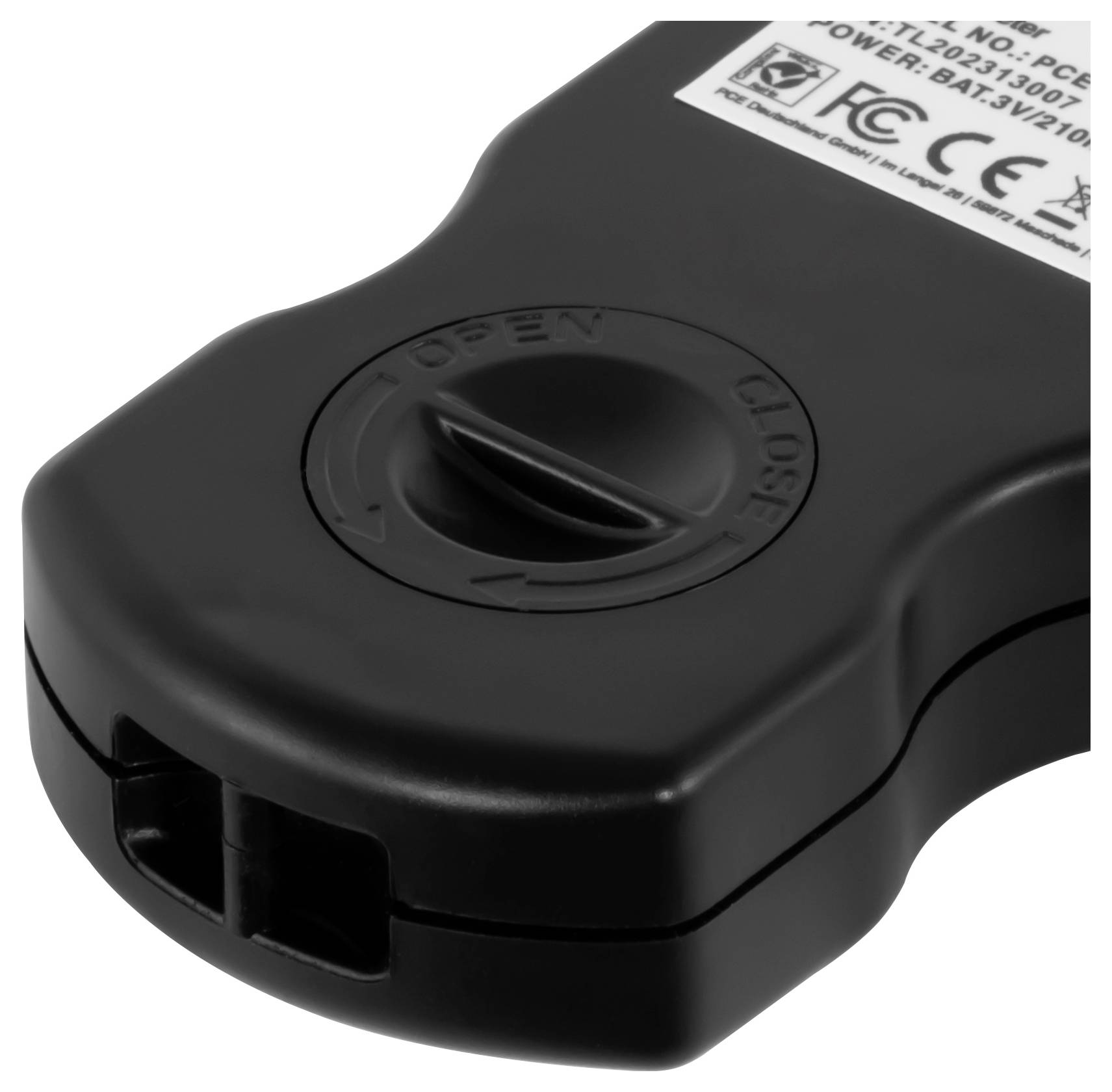 Nahaufnahme einer schwarzen Batteriefachabdeckung mit einem Dreh-Verschlusssystem "ÖFFNEN/SCHLIESSEN" und Produktetikett.