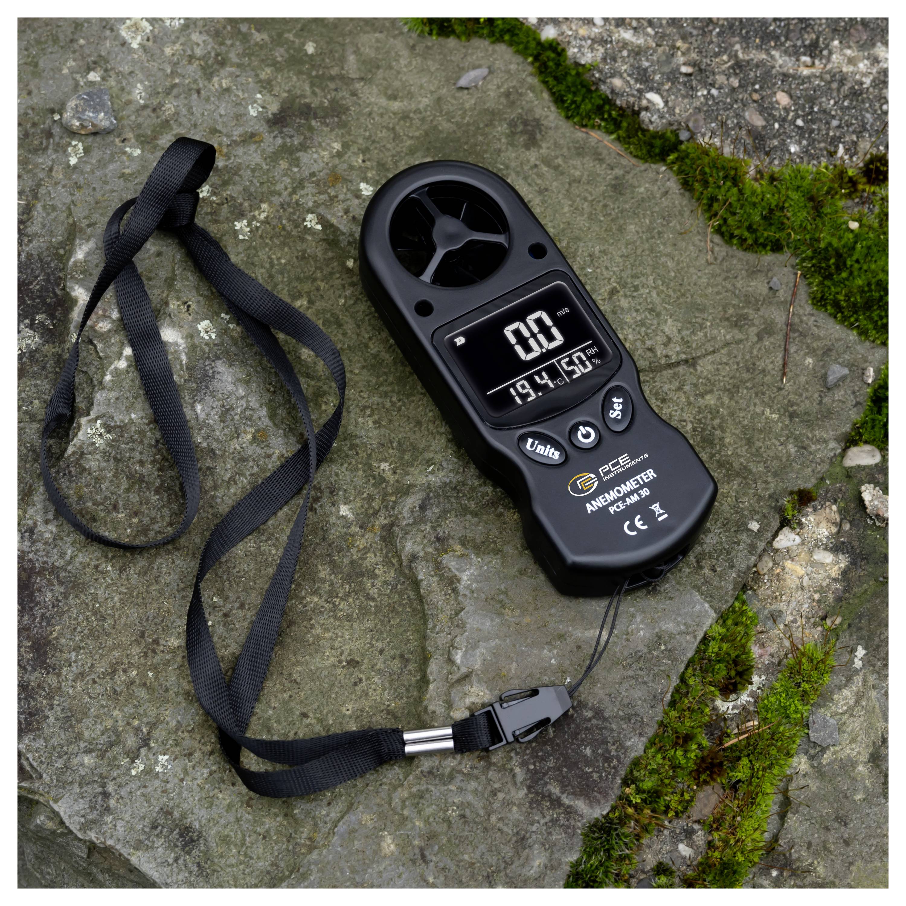 Tragbares Anemometer auf einem Stein mit befestigtem Riemen; das Display zeigt 0,0 und 19,4°C an und gibt damit eine Windgeschwindigkeitsmessung an.