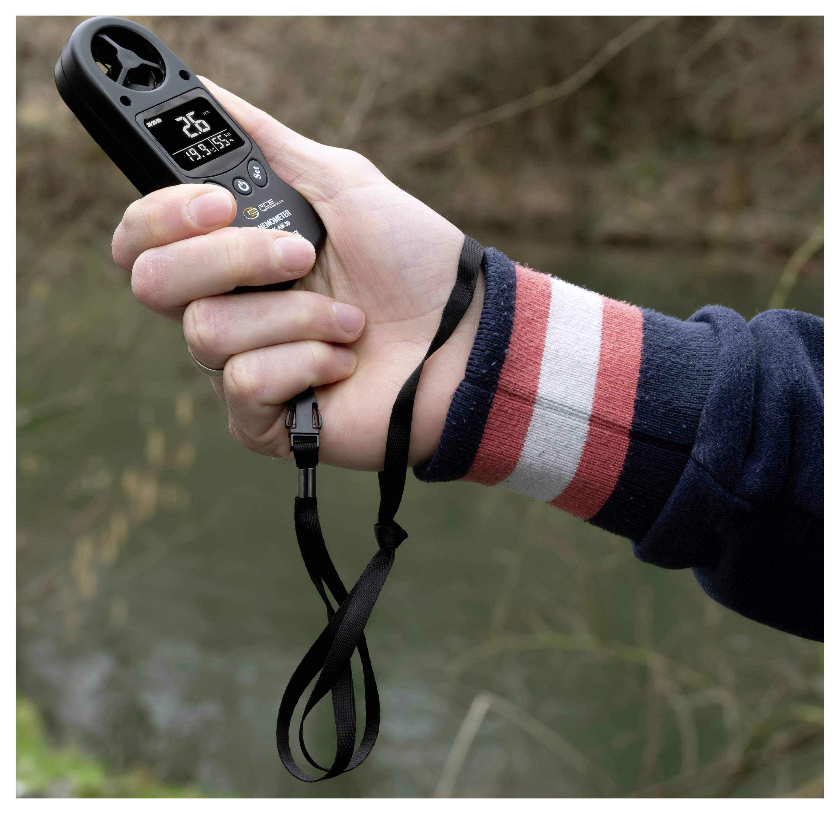 Hand hält ein tragbares digitales Anemometer im Freien, das auf dem Display eine Windgeschwindigkeit von 2,6 anzeigt.