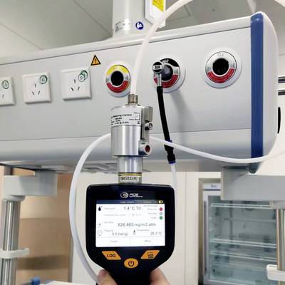 Eine Hand hält einen digitalen Luftqualitätsmesser, der 526,465 mg/m³ inmitten eines Raumes mit detaillierter medizinischer Ausrüstung im Hintergrund anzeigt.