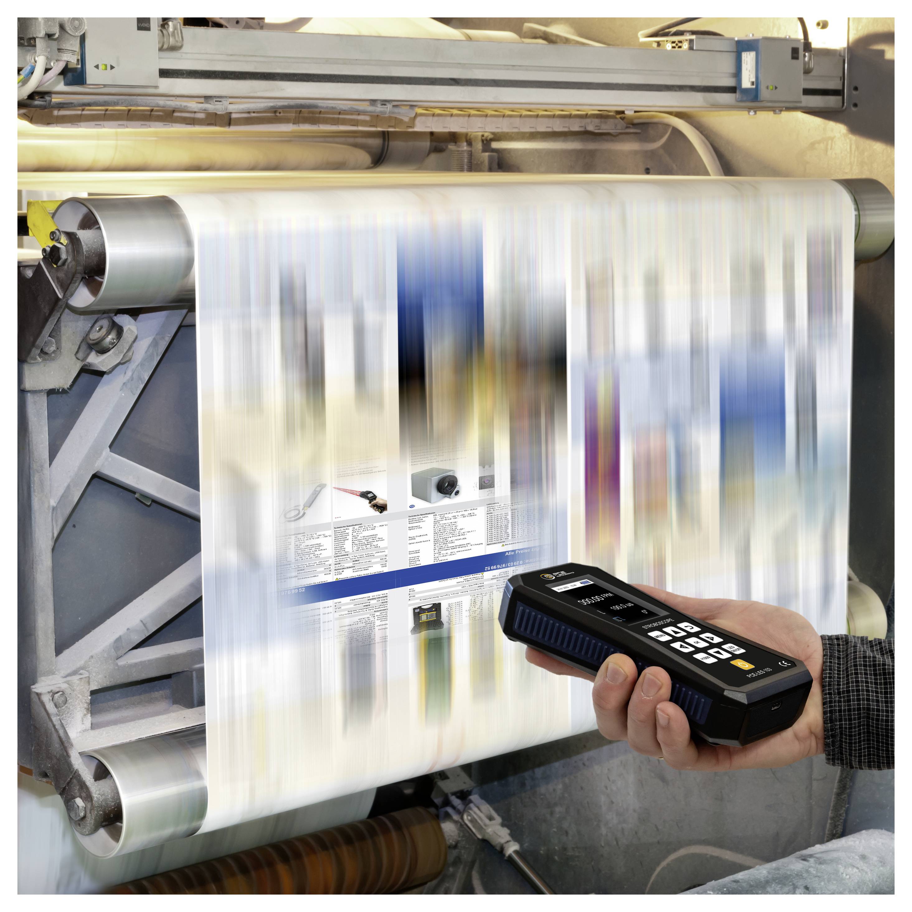 Druckmaschine produziert eine unscharfe Zeitungsrolle, während ein tragbarer Scanner das bewegliche Blatt inspiziert.