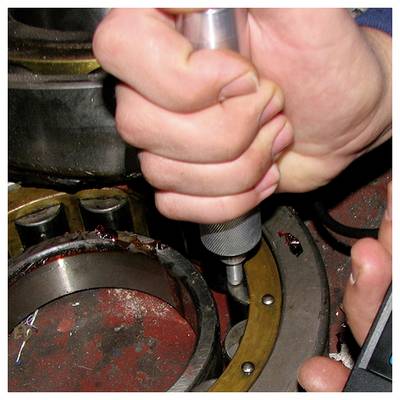 Nahaufnahme von Händen, die einen Schraubendreher verwenden, um ein mechanisches Teil in einer Maschine einzustellen.