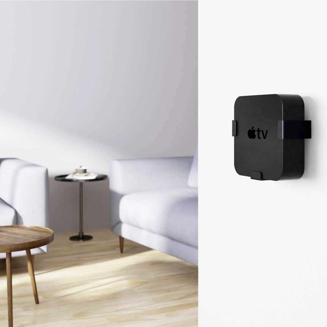 Eine schwarze TV-Box mit dem Apple-Logo ist an der weißen Wand eines modernen Wohnzimmers montiert. Im Hintergrund ein Tisch und ein Sofa.