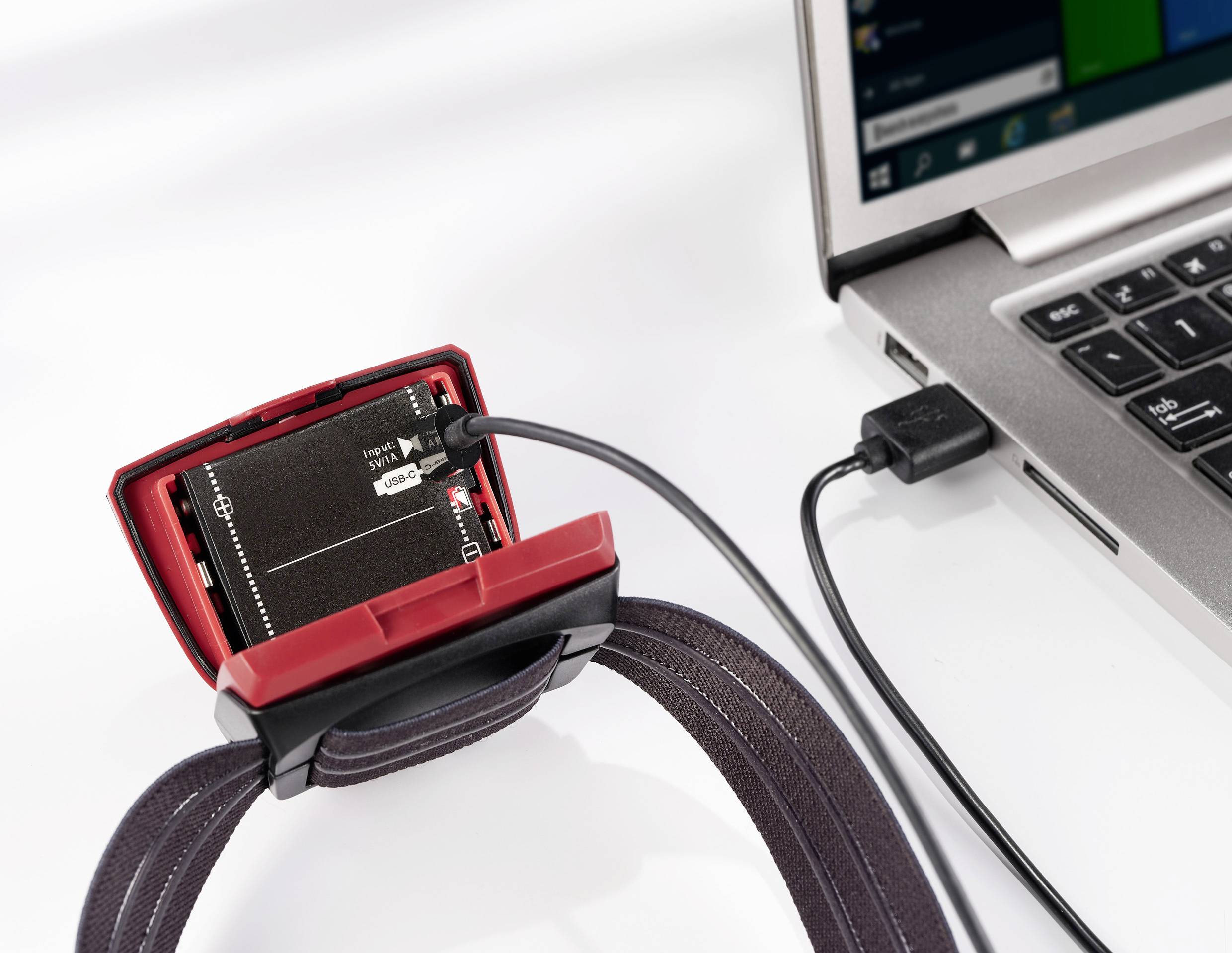 Ein elektronisches Gerät mit Kabel verbunden mit einem Laptop. Das Gerät hat ein Display und ist an einem Armband befestigt.