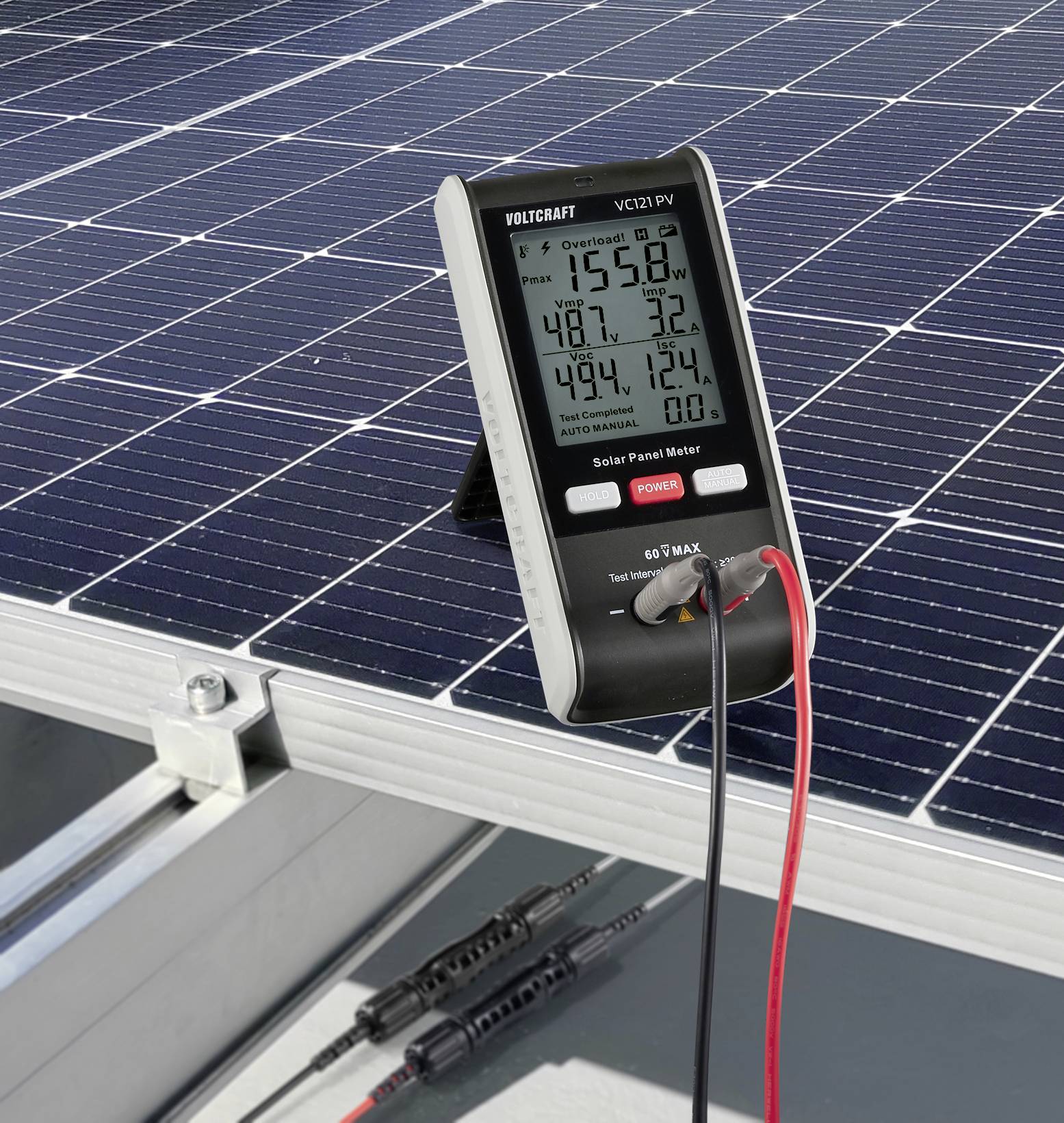 Digitales Messgerät zeigt Werte von Solarpanel an. Messgerät auf geneigtem Solarpanel mit Kabeln verbunden. Messwerte lesbar.