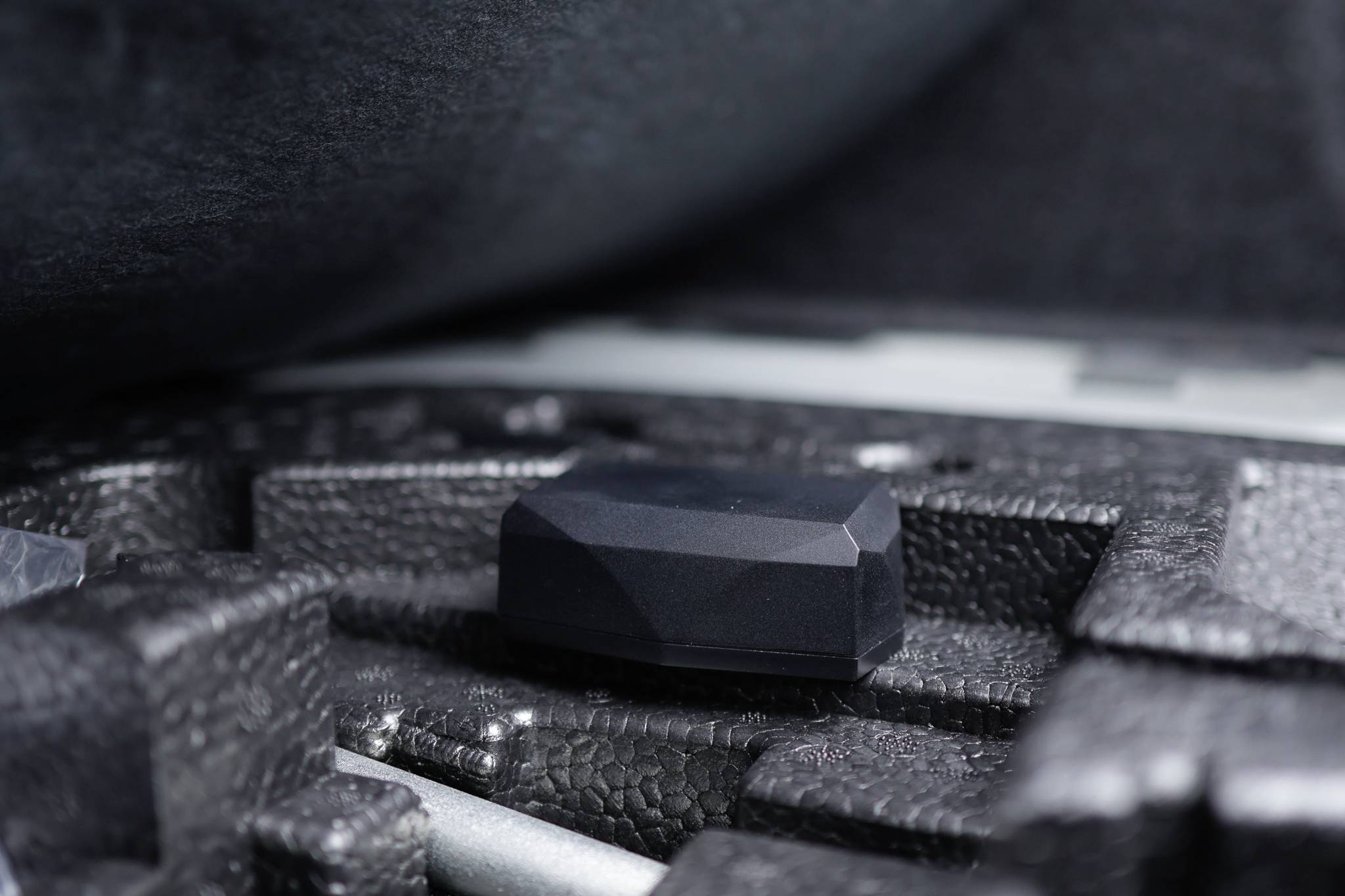 Ein schwarzes, facettiertes Objekt liegt in einer passgenauen Schaumstoffvertiefung in einem Koffer, umgeben von schützenden Materialien.