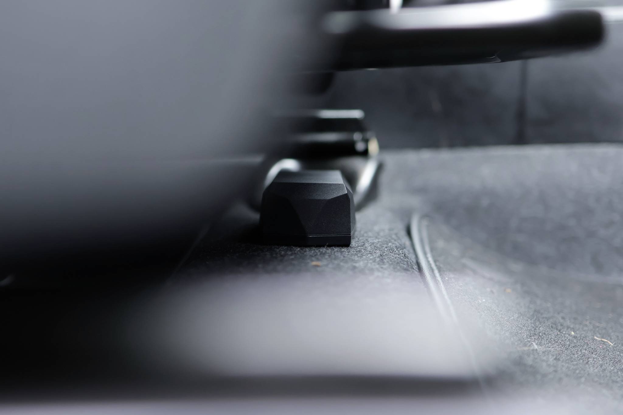 Unter einem Autositz ist schwarzes Plastikteil sichtbar, das möglicherweise ein Verstellhebel oder Befestigungselement sein könnte. Umgebung unscharf.