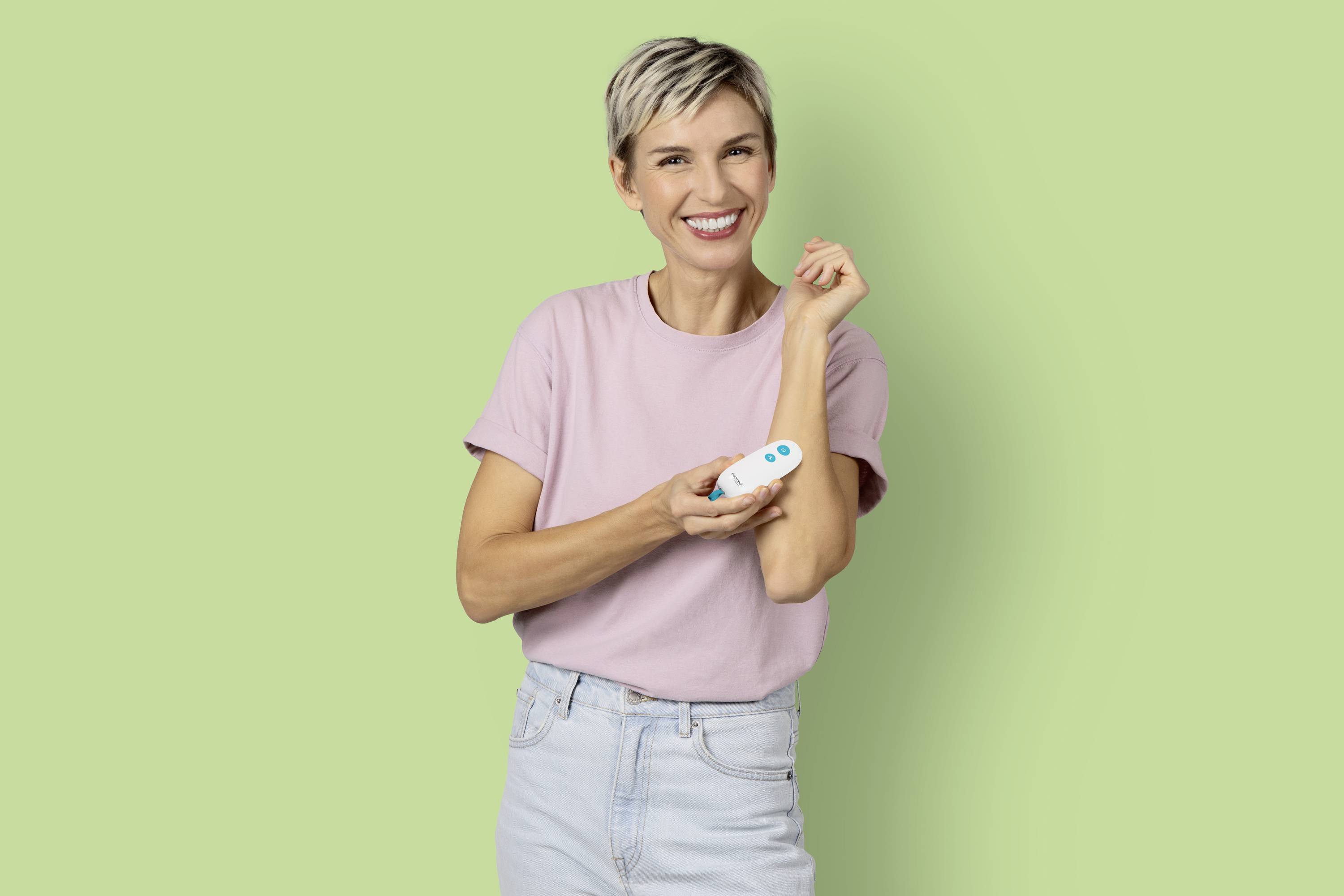 Frau in rosa T-Shirt lächelt, hält ein weißes Gerät in der Hand vor einem grünen Hintergrund.