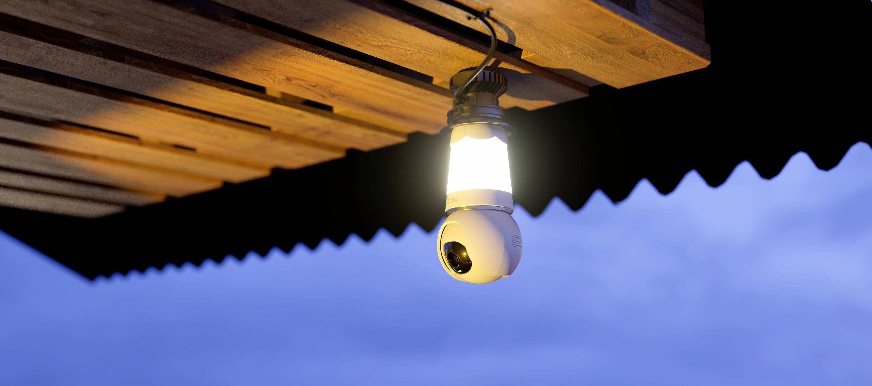 Eine Überwachungskamera mit integrierter Lampe ist unter einem Holzdach bei Dämmerung montiert und leuchtet.