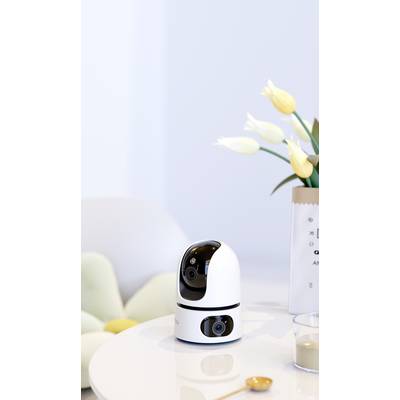 Eine Überwachungskamera steht auf einem Tisch neben einer Vase mit gelben Tulpen. Im Hintergrund ist ein helles Sofa zu sehen.
