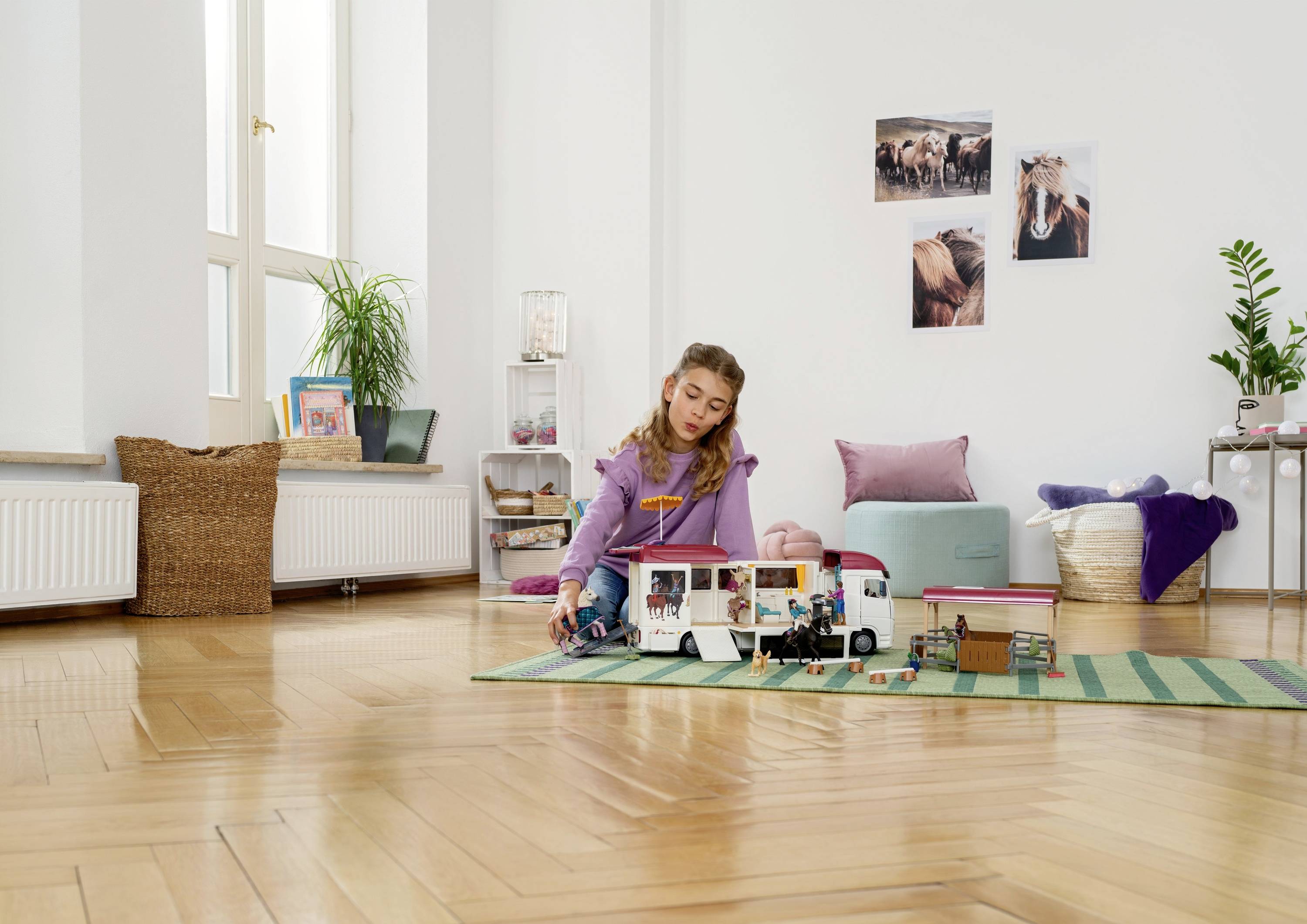 Ein Mädchen spielt in einem hellen Zimmer mit einem Puppenhaus, umgeben von Spielsachen. An der Wand hängen Tierfotos.