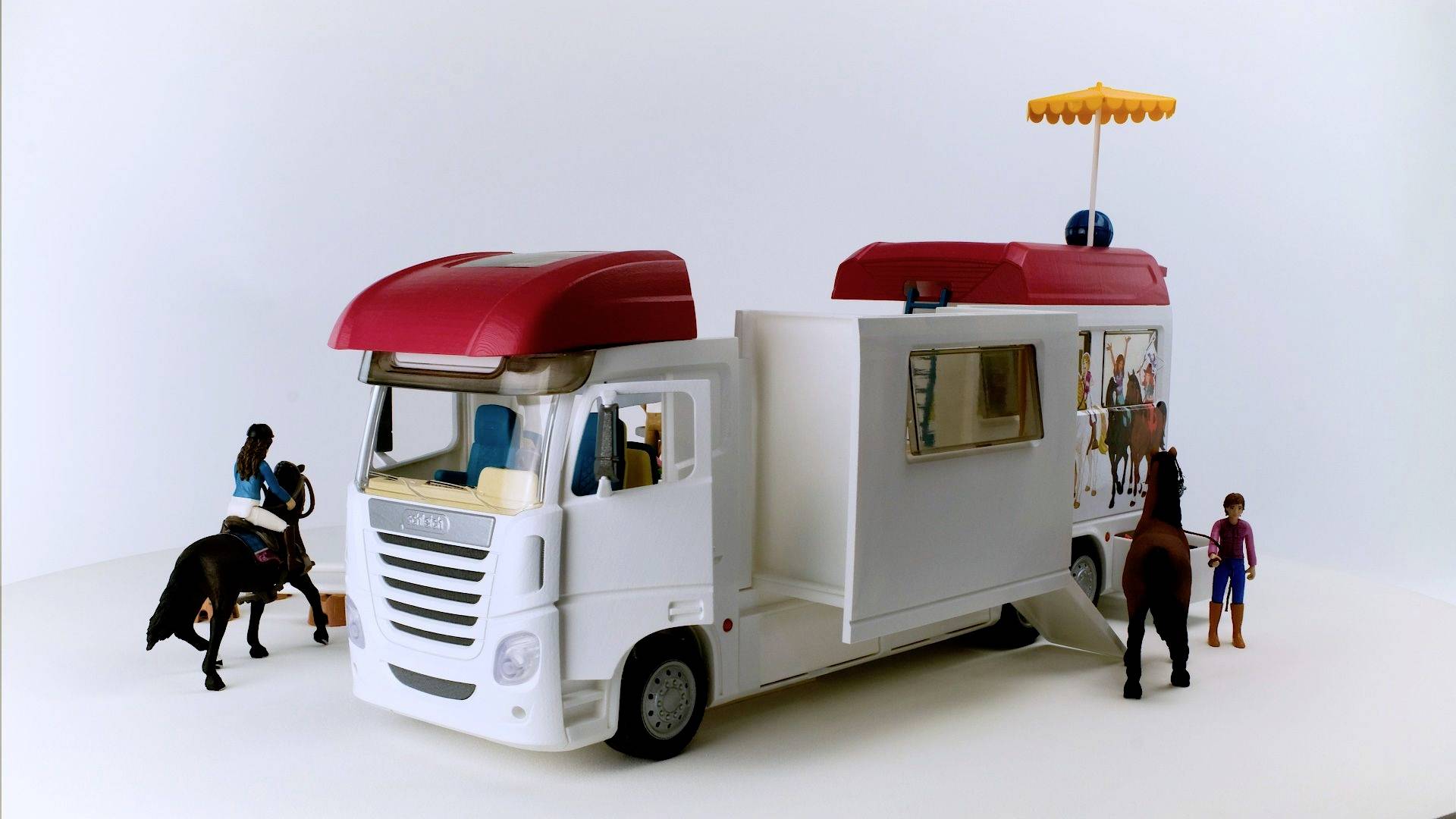 Ein Spielzeug-LKW mit ausziehbarem Wohnmobilteil, umgeben von Kinderfiguren und Pferden.