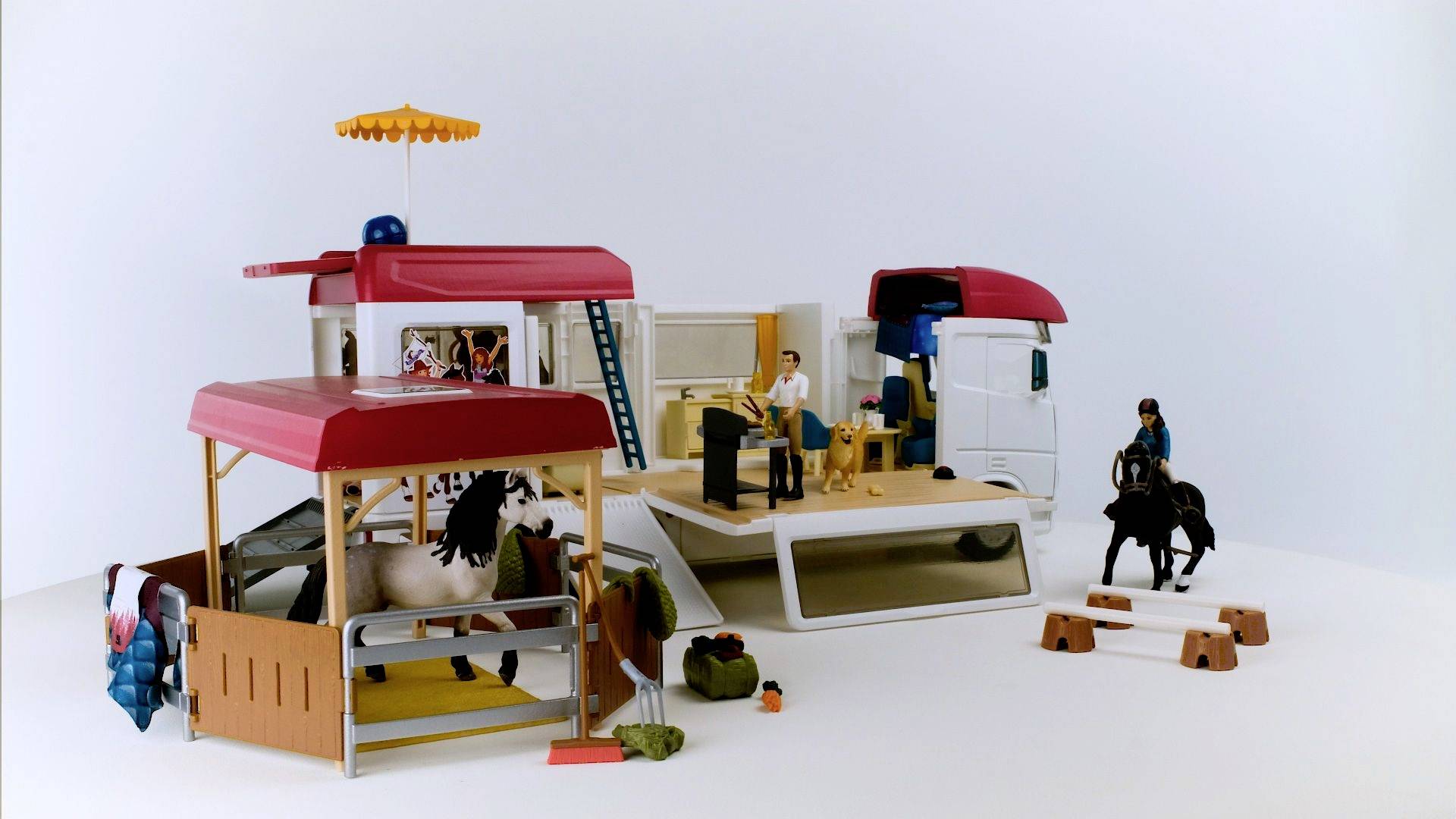 Spielzeug-Set mit Wohnmobil, Pferd, Person und Ausrüstung. Eine Figur sitzt drinnen am Tisch. Ein Pferd im offenen Bereich.