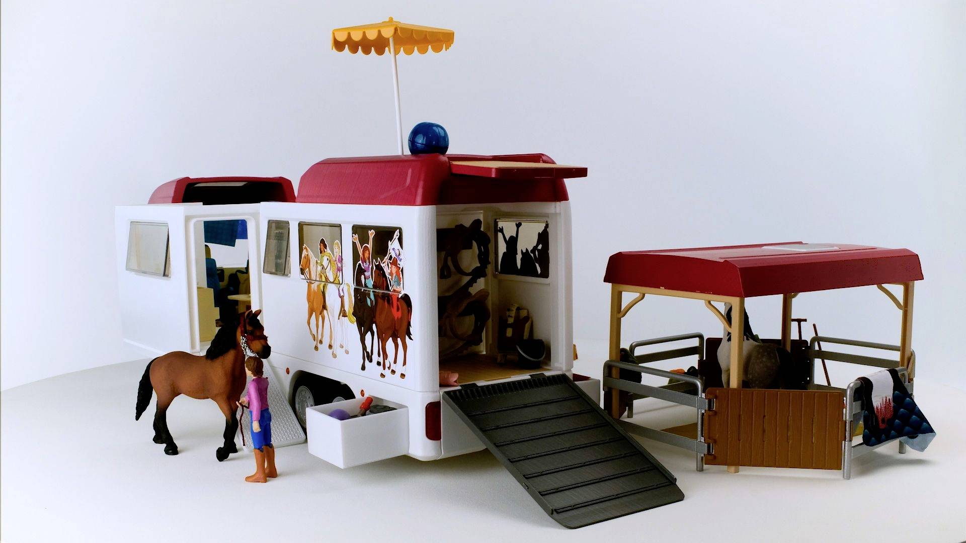 Ein Puppencamper mit Schiebetüren und Pferdeanhänger. Eine Figur steht neben einem Pferd. Der Anhänger hat ein offenes Dach und ein Tor.