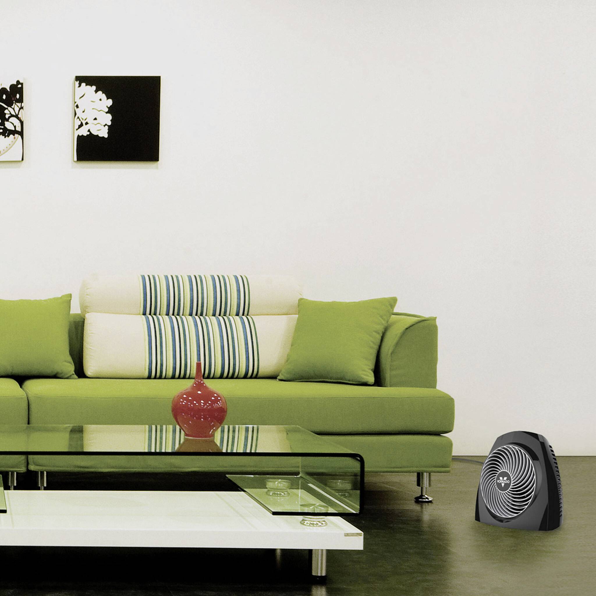 Ein modernes Wohnzimmer mit grüner Couch, rotem Dekoglas auf einem Glastisch und Bildern an der Wand. Im Hintergrund ist ein Luftreiniger.